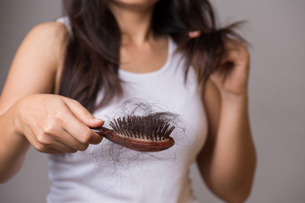 Frau mit einem Kamm in der Hand, auf dem viele Haare liegen