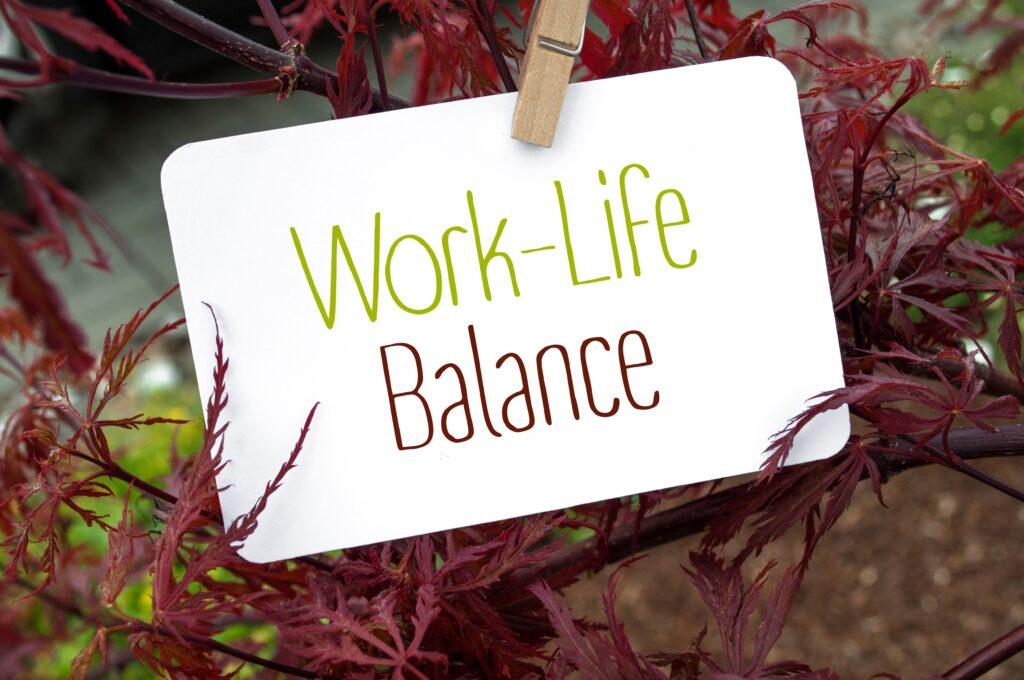 Familien Service: Eine weiße Karte mit der Aufschrift „Work-Life Balance“ hängt an einer Holzklammer zwischen roten Blättern