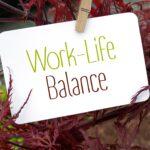 Familien Service: Eine weiße Karte mit der Aufschrift „Work-Life Balance“ hängt an einer Holzklammer zwischen roten Blättern