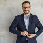 Laechelnder Mann im Anzug vor grauer Wand | Kryolipolyse Behandlung